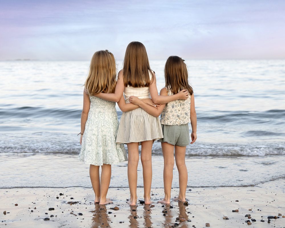Children holding each other while looking out at the ocean during a coastal Massachusetts beach photography session